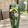 Green Stanley tumbler with a yellow ribbon and charm on a wooden table outdoors.