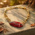 Gold bracelet with a red and black stone on a stone surface with leaves.