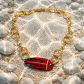 Gold bracelet with a red and black patterned charm on a sandy background