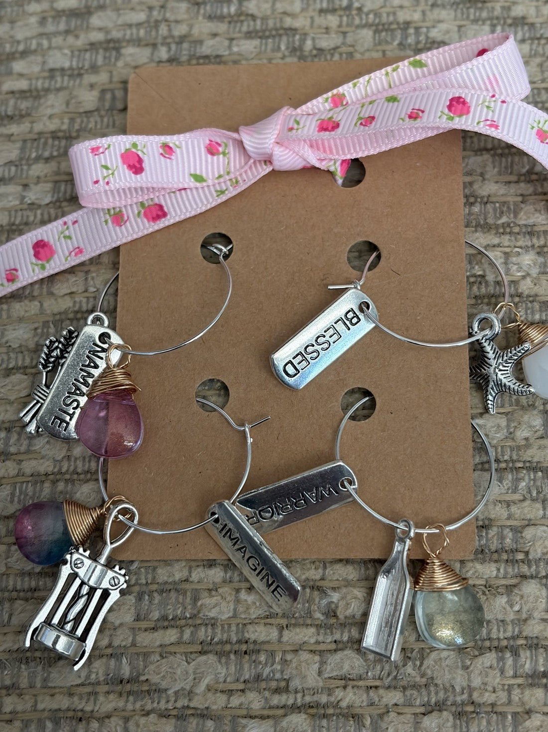Handmade glass bottle charms featured on a gift card with floral ribbon and various gemstone accents.