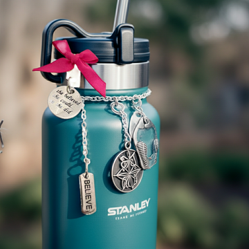 Handmade Blue Stanley water bottle with charms and a pink bow on a blurred natural background